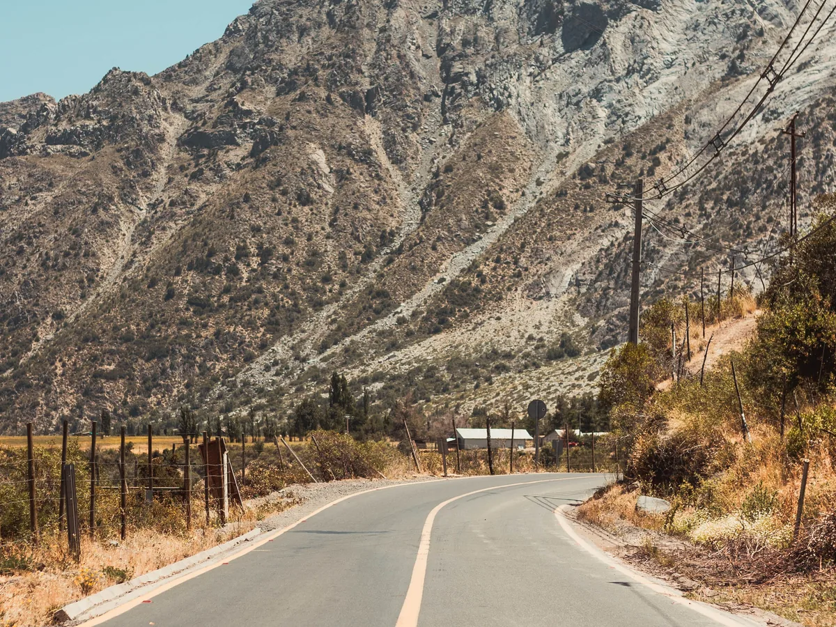 A paved mountain road climbing through dry Andean foothills near Santiago, representative of the drive up Cajon del Maipo